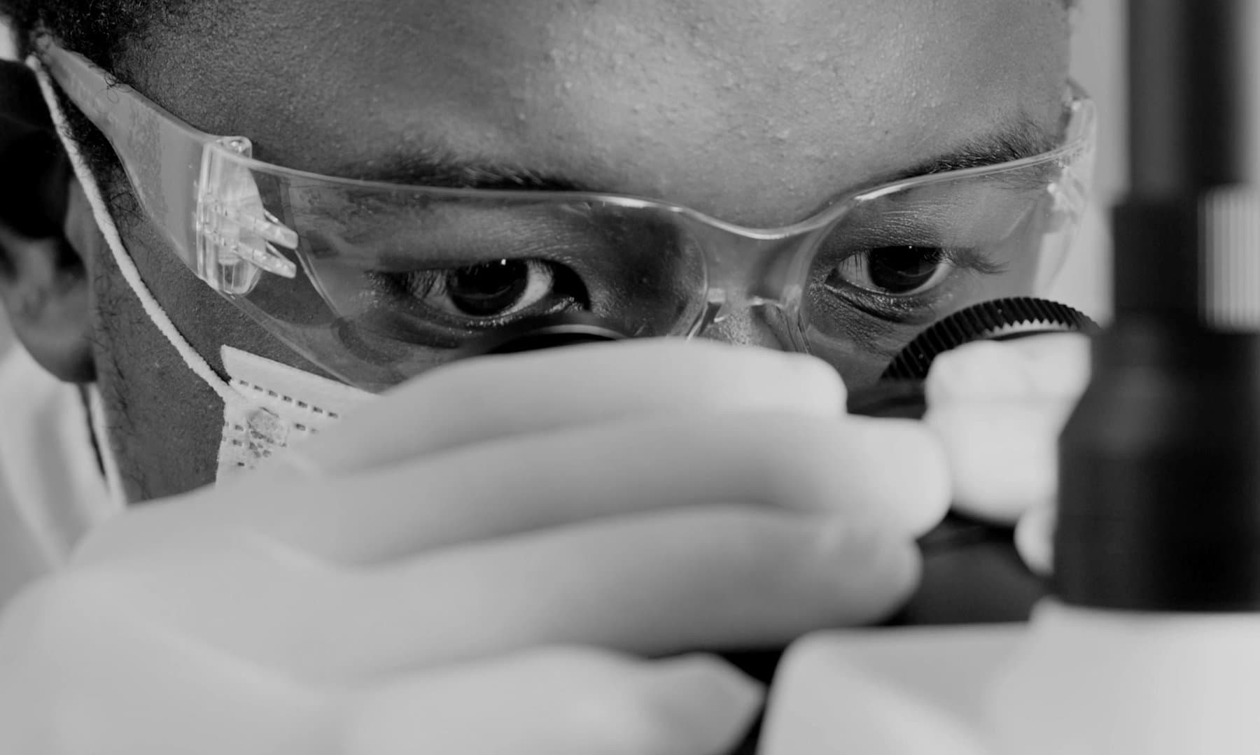 A scientist examining samples under a microscope with precise focus — the clinical precision behind LifeVitals.